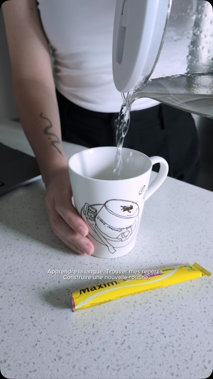 Khami pours water into a white mug beside a yellow Maxim coffee sachet
